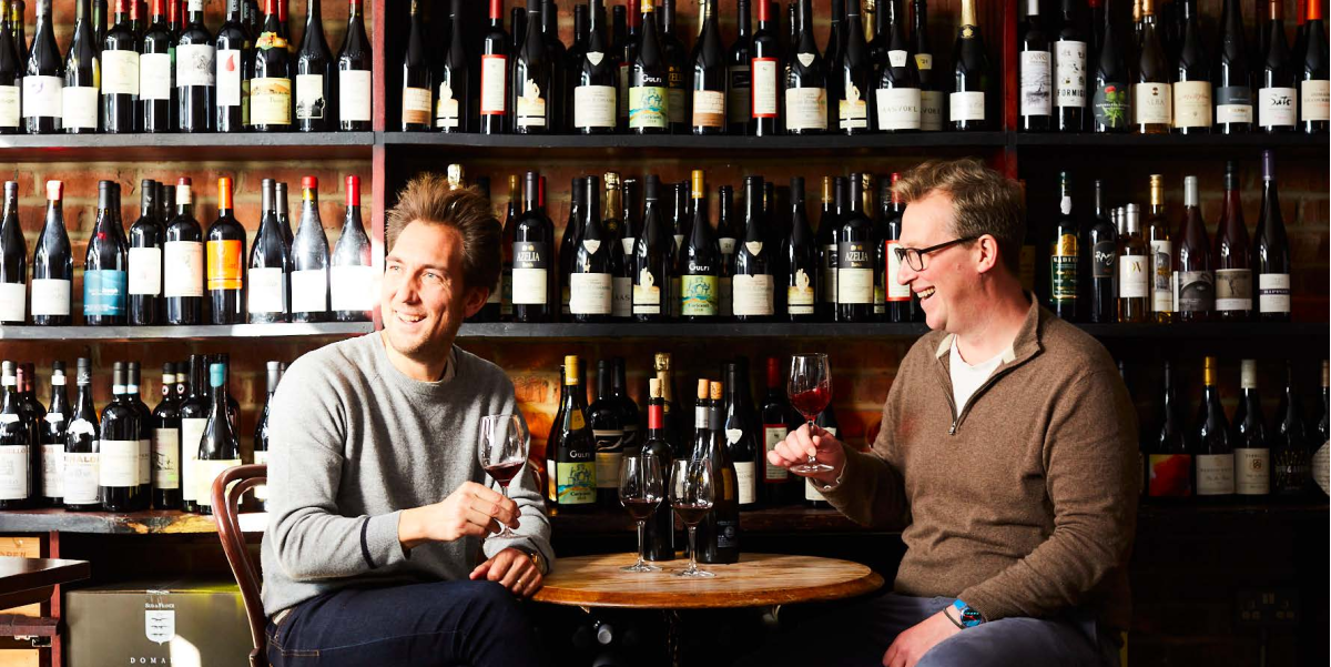 The 10 Cases wine bar in London — two hosts enjoying wine in front of an extensive bottle wall
